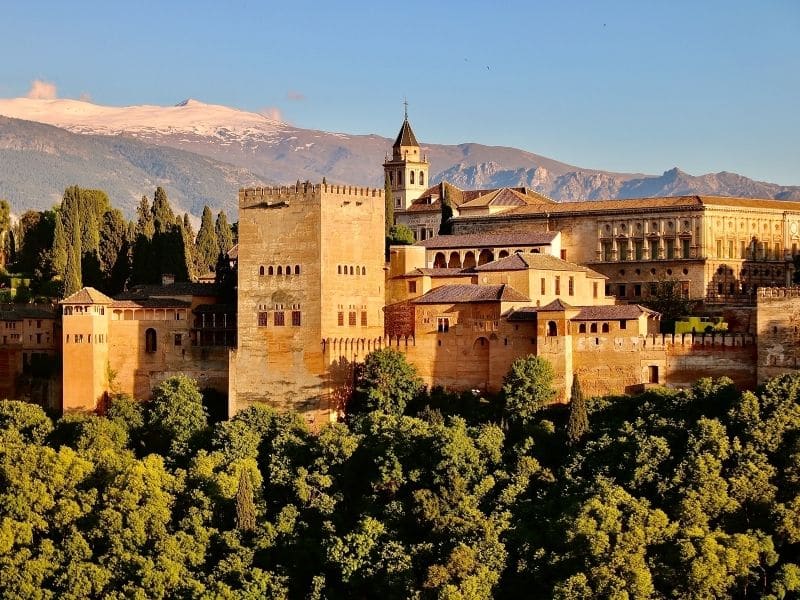 The Alhambra  sits atop a hill in Granada with the snow capped mountains behind. 