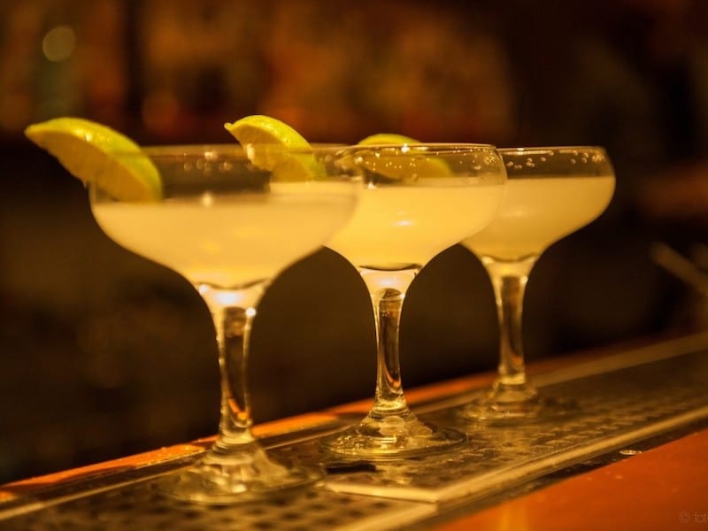 Three margarita cocktails on a bar with wedges of lime for garnish